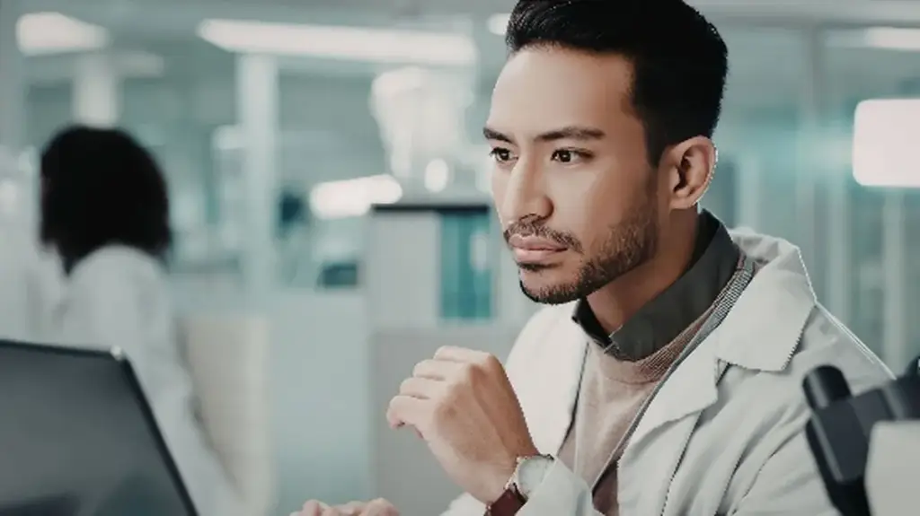 Scientist in a laboratory coat looking thoughtfully at a screen